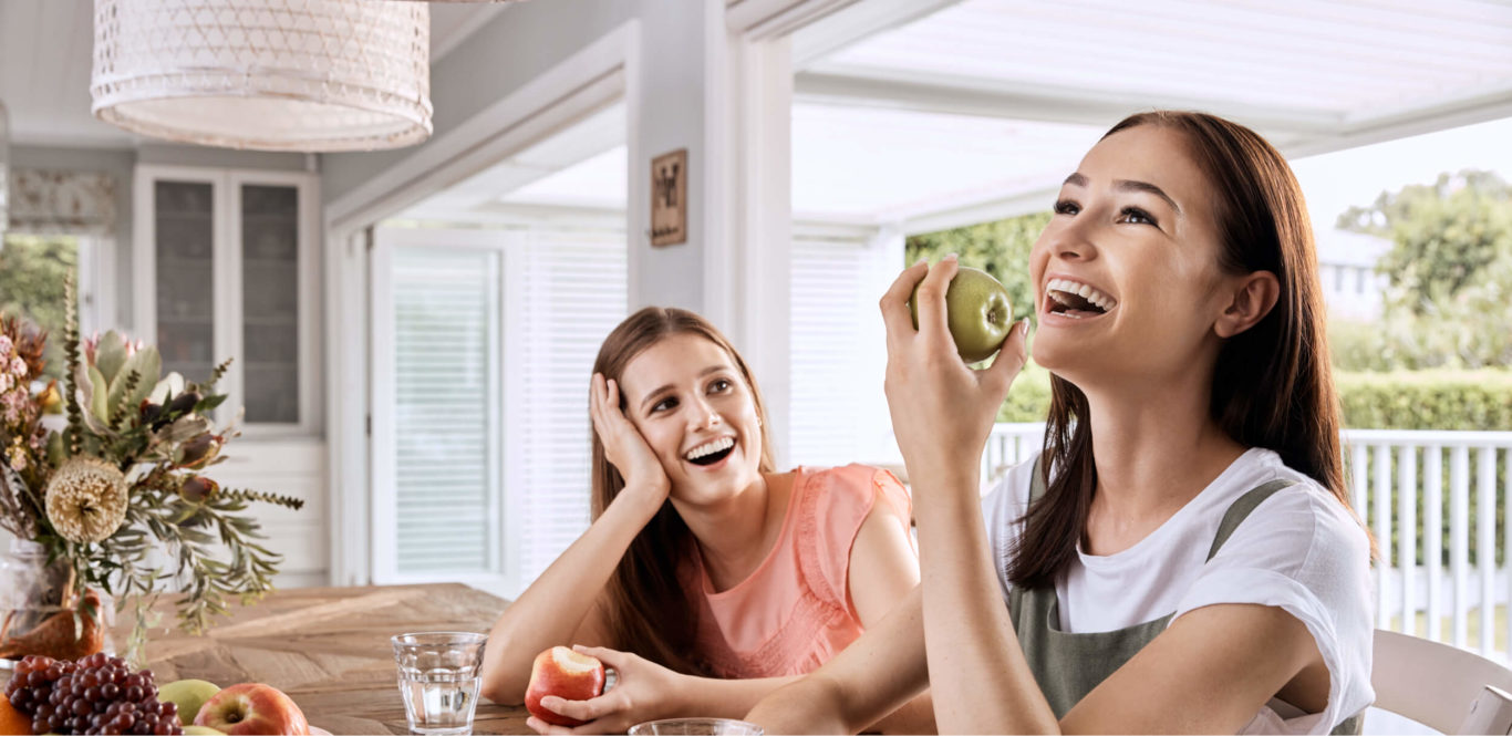Two women sharing a laugh while enjoying apples.