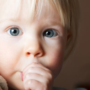 A blond hair child sucking his thumb.